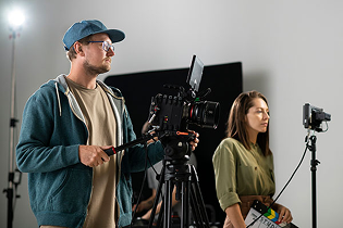 A cameraman filming an actress or interviewee on a professional film set with lighting equipment.